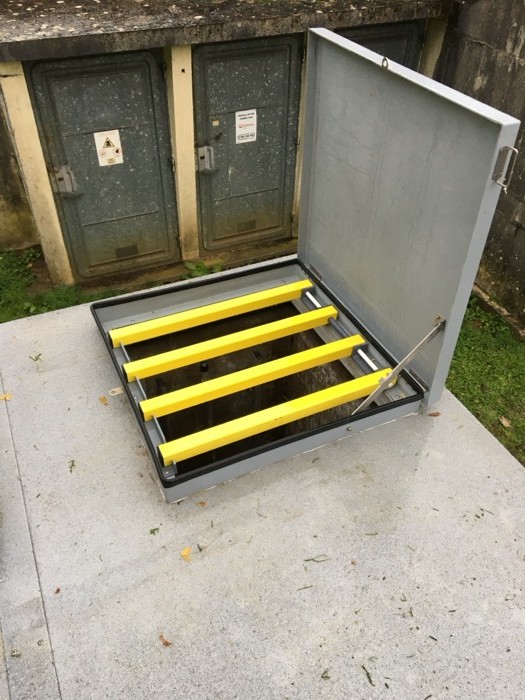 Trappe composite ouverte sur une dalle extérieure, grille anti-chute à barreaux jaunes